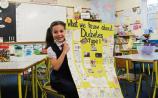 Ellie Noone, 7, proudly shows off the collaborative poster project she has completed in school