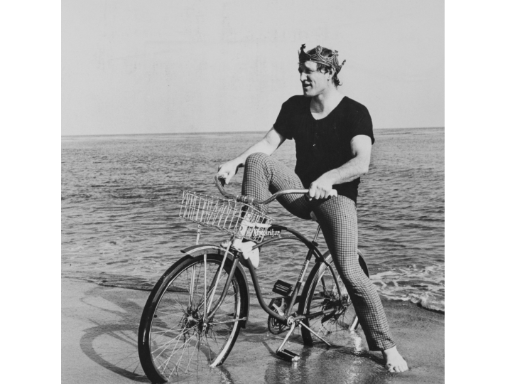 Richard Harris pictured sitting on a bicycle with a crown on his head on a beach at the waterside                      PICTURE: Richard Harris Archive, Ucc