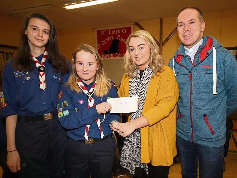 Scout member Aoibhinn Daly presents Katie Whelan, Lisa's Light with €445, alongside Jessica Rennicks and Fr Derek Leonard in the Shannon Banks scout hall
